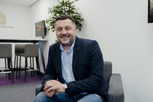 A man wearing a shirt and jacket sat down smiling at the camera
